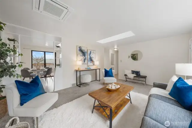 The living room flows into the dining area through an open shelving divider that adds style and function. Notice the recessed ceiling mini-split system, offering efficient heating and cooling for year-round comfort.