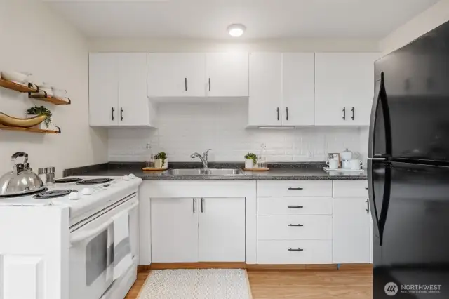 This kitchen features timeless white cabinetry paired with a durable laminate floor for easy maintenance and a clean look. A classic appliance package offers reliable functionality.