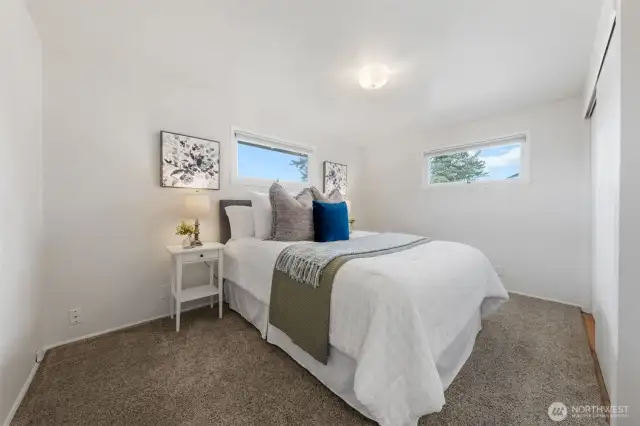 Bedroom One, features two horizontal windows that bring in natural light while maintaining privacy. Soft carpet and neutral walls offer a relaxing and versatile space.