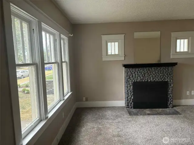 The wood-burning fireplace is the heart of this bright and beautiful living room and all its charm. wide baseboards and wood details remain from time gone by.