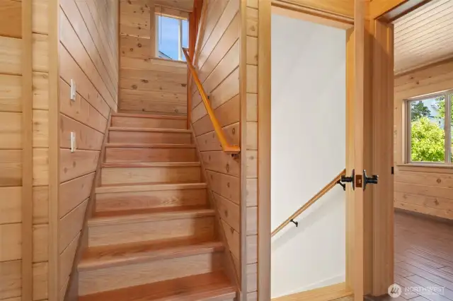 Stairwell leading up to Primary and stairs leading down to storage & garage. One of 2 main level bedrooms to the right. All flooring is tile radiant heated - top of the line!