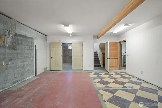 Lower level room shows view toward garage & workshop, stairs up to kitchen and to the right, laundry & unfinished bathroom.