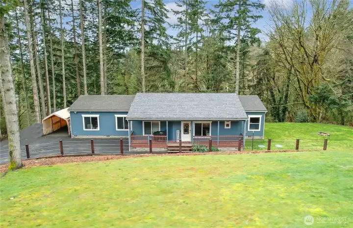 Private 1-level home on acreage with covered porch, lush lawn, and peaceful wooded backdrop.