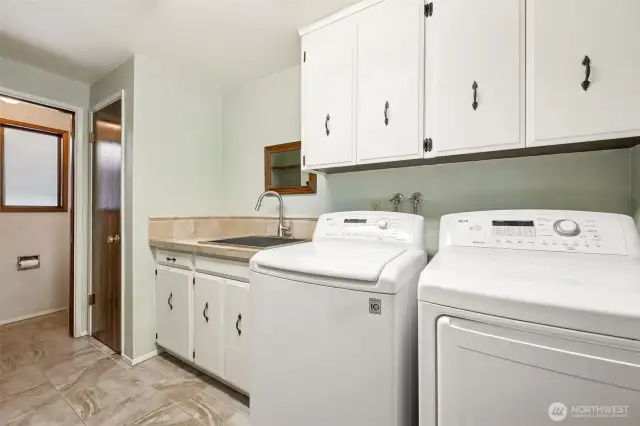 This main-floor laundry room delivers more than just a place to toss a load. Cabinet storage, counter space, a deep closet, and a utility sink make it genuinely functional, and yes, there’s even a private toilet tucked behind a door with a privacy glass window.