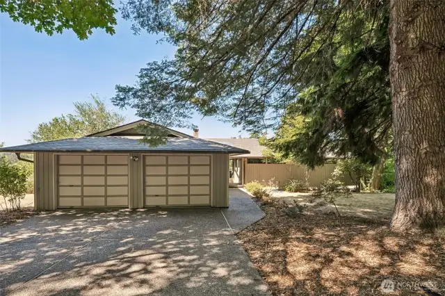 The two-car garage sits just off a wide, level driveway, with an easy, no-step transition to the walkway and front door. It’s a thoughtful layout that makes daily life simpler, especially when rain, leaves, or icy weather roll in. A tall evergreen shades the entry with soft, dappled light and brings a touch of natural drama to the front yard.