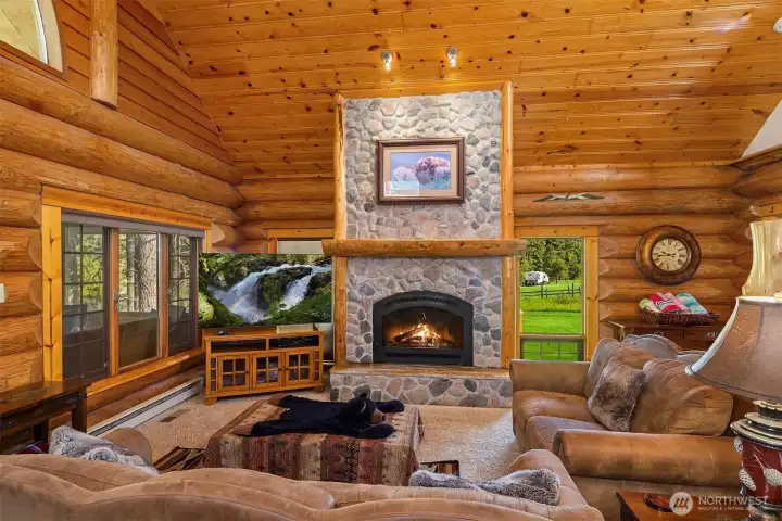 Great room with soaring wood ceilings, a stunning river rock fireplace, and expansive windows bringing in natural light and scenic views—perfect for gathering and relaxing.