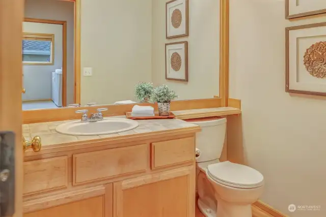 A well-placed half bath offers convenience and style, featuring a wood-trimmed vanity, tile countertops, and a large mirror. This space is ideal for guests and everyday use.