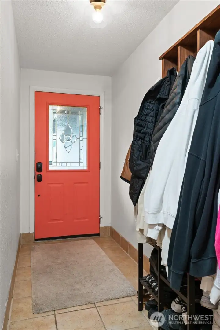 Bright entryway with tile flooring, coral front door, and coat storage.