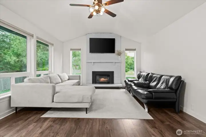 Spacious living room with large windows, vaulted ceiling, and fireplace focal point.