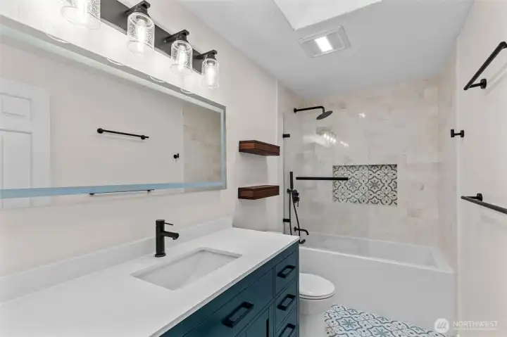 Stylish hall bath with blue vanity, tile tub/shower and patterned niche.