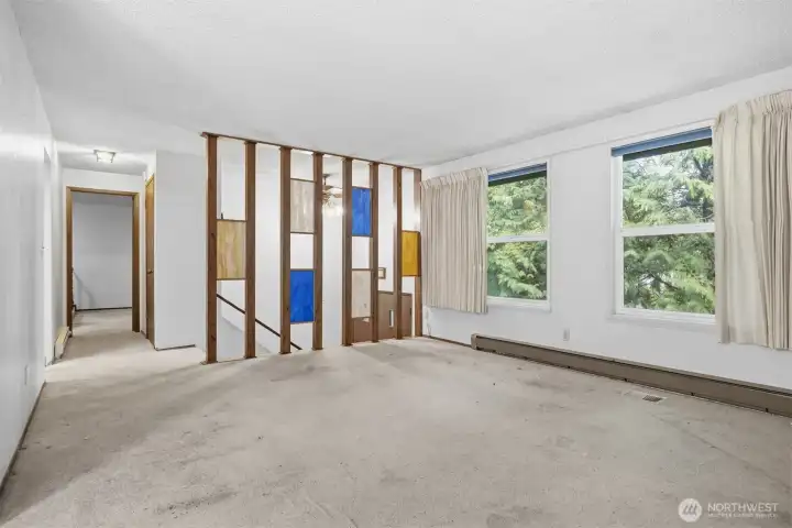 Looking across the living room with the stained glass wall that is at the stairway to the entry and the basement. The primary bedroom and full bath are down the hallway.