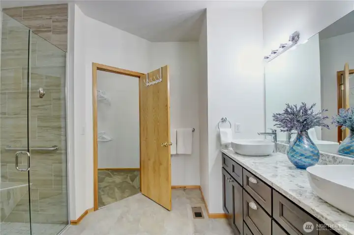 Tastefully updated primary bathroom with dual sinks, beautifully tiled walk-in glass shower, and a spacious walk-in closet.
