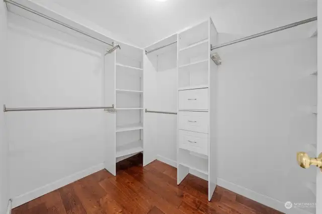 Walk-in closet with built-in shelves and hardwood floors.