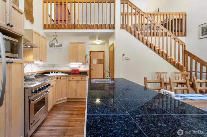 Kitchen with large granite peninsula, double sink, hardwood floors, and open view to dining and loft.