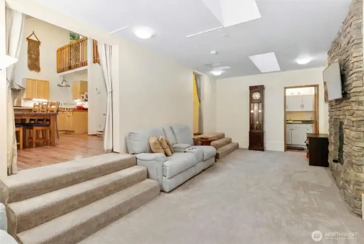 Lower-level family room with stone fireplace, carpet floors, and steps up to main living area.