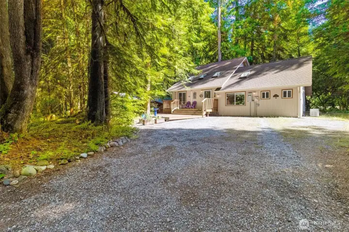 Front exterior with deck seating, skylights, and large gravel parking area.