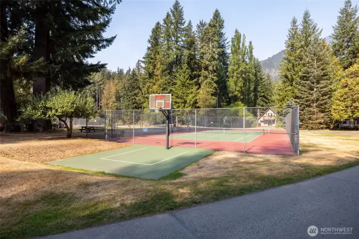 Community open field with picnic tables and volleyball net surrounded by trees.