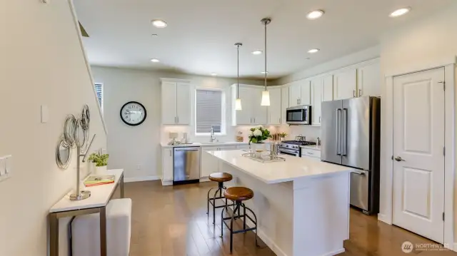The kitchen has been beautifully designed with hardwood floors, a large center island with eating bar and ample quartz counters, a pantry and just the right amount of modern lighting.