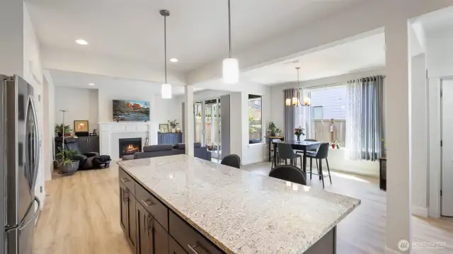 Bright and welcoming modern open-concept kitchen and living space featuring a granite island, stainless steel appliances, and cozy seating with natural light streaming through the curtains