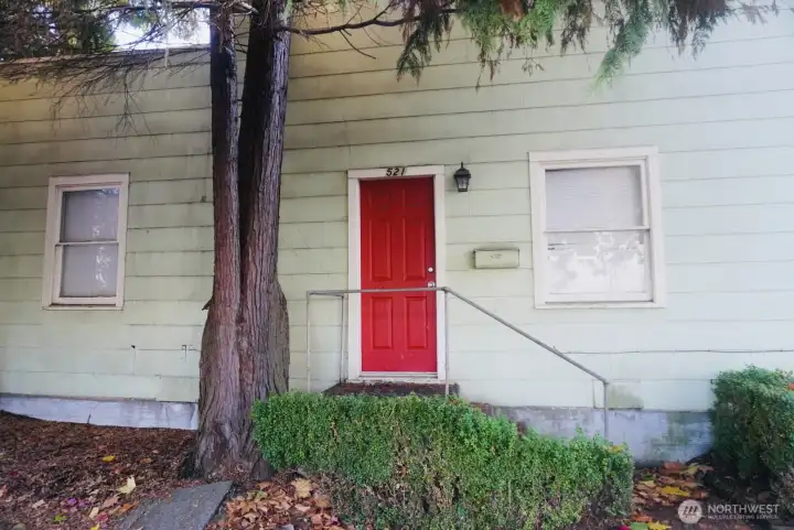 Lower-level unit with convenient street-level access, featuring a charming red entry door and mature landscaping for added privacy.