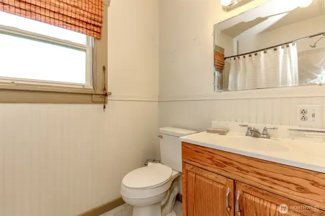 Bathroom has full sized bathtub with shower, overhead light fixture and wall mounted light fixture adjacent to outlet.