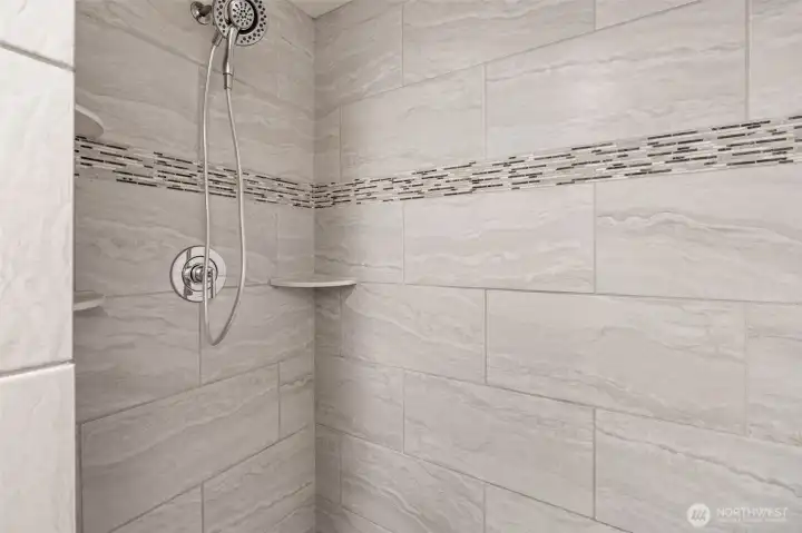 Shower boasts a detachable shower head and sleek tile finish, combing modern style with practical functionality.