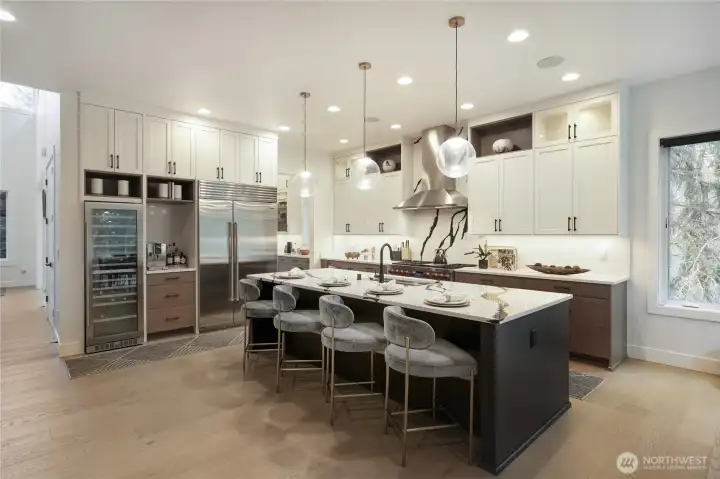 This designer kitchen blends modern elegance with everyday functionality. An expansive island with seating for five anchors the space, complemented by rich wood accents, sleek white cabinetry, and wide-plank flooring. A professional-grade Wolf range with a statement hood, Sub-Zero refrigerator, and built-in wine cooler elevate both style and performance. Bright, inviting, and impeccably finished, it’s the perfect setting for cooking, gathering, and entertaining.