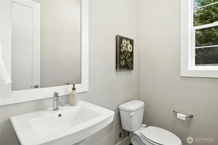 The main-level powder room features a clean, modern design with a pedestal sink, sleek fixtures, and bright natural light. Thoughtfully positioned for guests, this space blends simplicity and style with refined finishes that complement the home’s contemporary aesthetic.