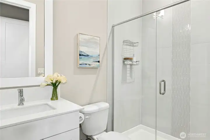 The guest bathroom features a sleek vanity, quartz countertop, and contemporary fixtures that reflect the home’s cohesive modern design. A glass-enclosed shower with clean tile surround adds both style and functionality, creating a comfortable and well-appointed space for visitors.