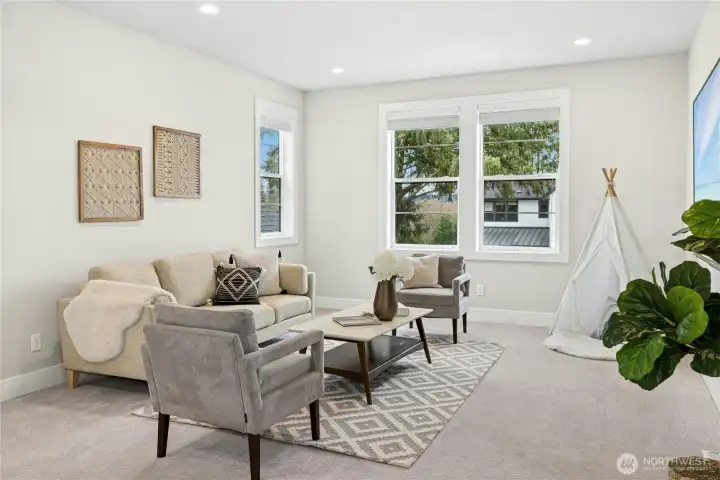 A closer view of the upper-level bonus room highlights its comfortable layout and flexible design, ideal for a media space, playroom, or home office. Large windows invite natural light while maintaining a bright, welcoming atmosphere throughout this versatile retreat.