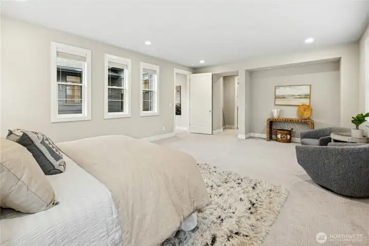An alternate view of the primary suite highlights its impressive scale and flexible layout, offering ample space for a sitting area or private retreat. Soft carpeting, recessed lighting, and multiple windows create a tranquil atmosphere that feels both spacious and inviting.