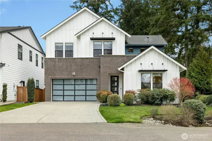 Striking modern farmhouse exterior with board-and-batten siding, brick accents, and a contemporary glass-paneled garage door. Thoughtful landscaping and clean architectural lines create exceptional curb appeal in Winslow Grove.