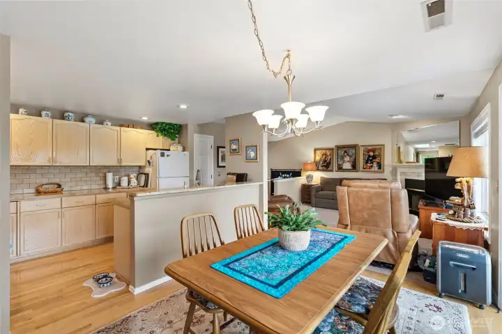 An open-concept view from the dining room featuring sightlines into the beautifully updated kitchen and back toward the spacious main living room highlighted by a cozy wood-burning fireplace.