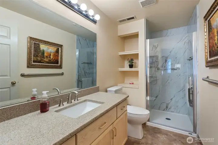 Primary bath featuring modern quartz countertop, a sleek no-edge sink, and durable tile flooring. The space includes a recently remodeled shower and custom built-in shelving, offering both style and functional storage.