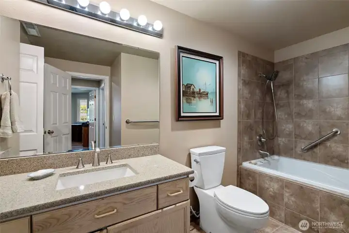 The main guest bathroom includes beautiful tile flooring, a soaking tub with tile surround, quartz countertop with no-edge sink, and a skylight.