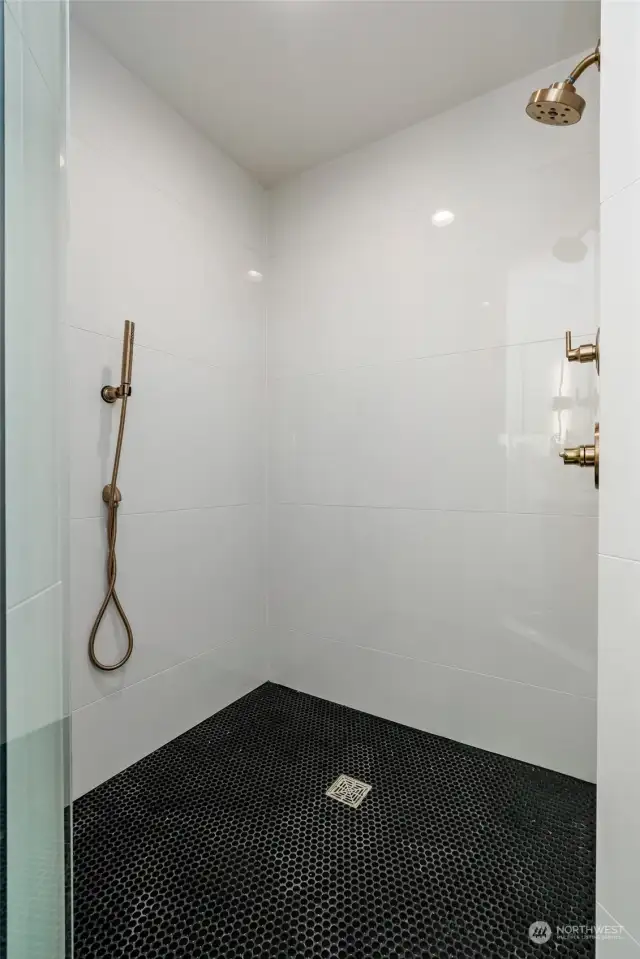 Experience ultimate convenience and style in this tiled shower, featuring both a fixed shower head and a separate handheld option.