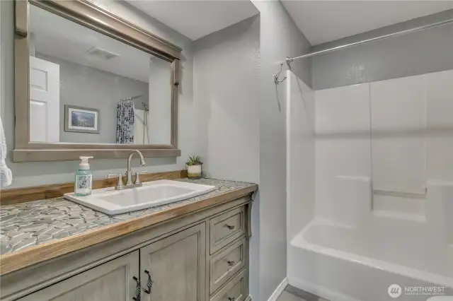 The full bathroom has a unique, beautiful, rock custom countertop! The tub fixtures are new, and you won't miss the additional storage behind the bathroom door!