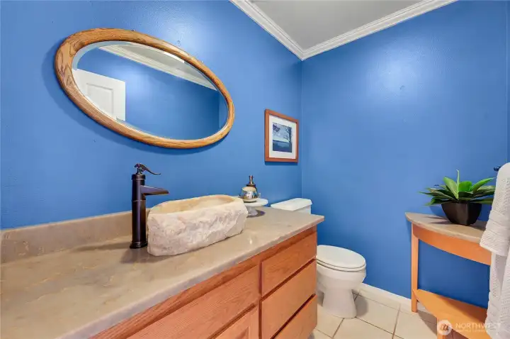 Powder room with bold blue walls, stone vessel sink, and updated faucet—stylish half-bath for guests near front door