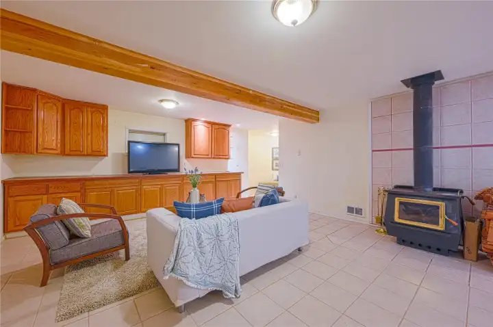 Expansive lower-level living space anchored by a cozy wood stove and exposed beams, offering flexible room for a second living area, hobby zone, or guest suite with easy, low-maintenance tile floors. Expansive lower-level living space anchored by a cozy wood stove and exposed beams, offering flexible room for a second living area, hobby zone, or guest suite with easy, low-maintenance tile floors.