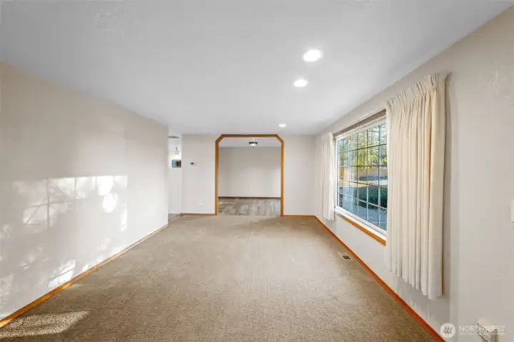 Empty living room shown from another angle, open to the dining room with views to the front of the home