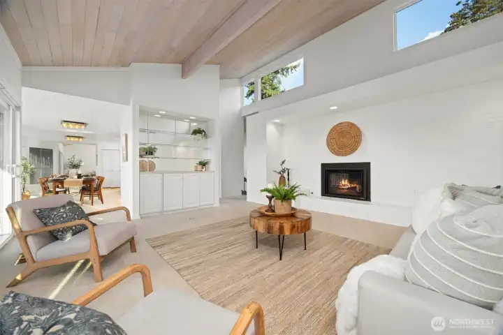 The wooden ceilings are carried through in the living room with the clerestory windows above the fireplace wall that bring in so much natural sunlight from the south. There is also a bar or entertaining area to the left.