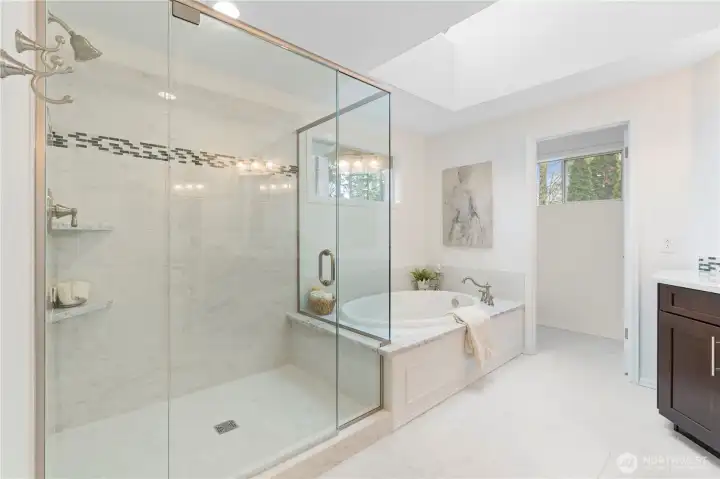 The primary ensuite bathroom feels truly luxurious, featuring a glass-enclosed shower, marble countertops, a marble tub surround, tile flooring, a private water closet, and a skylight that fills the space with natural light.