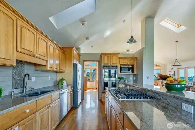 Designed for the modern cook who loves to entertain—this wide galley-style kitchen boasts granite countertops, gas cooktop, double ovens, and skylights that flood the space with natural light, all seamlessly connected to the dining and living areas.