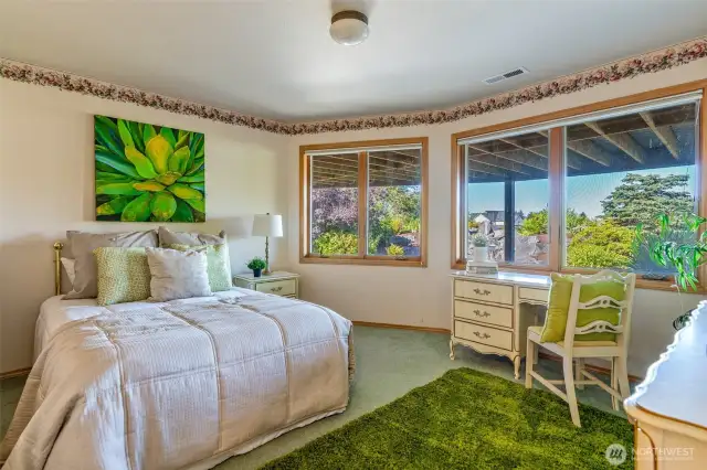 A bright and inviting downstairs bedroom with large windows that frame colorful landscape views—perfect for guests, teens, or as a quiet retreat.