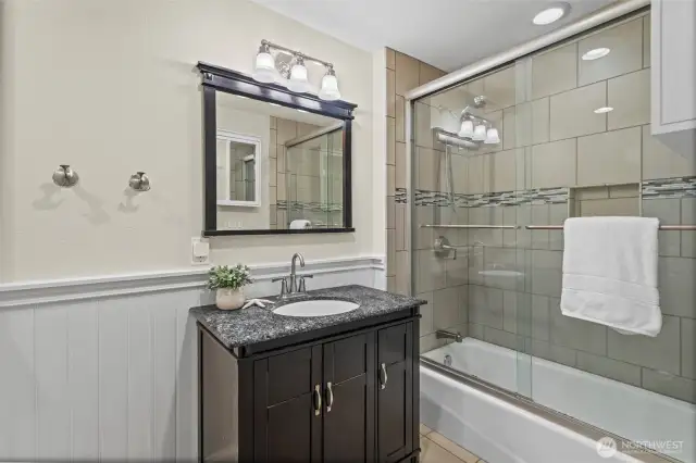 This main floor bathroom offers beadboard details as well as a tile floor, updated vanity, and a full tile tub and shower surround with glass sliding doors.