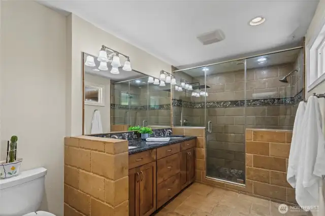 The primary bathroom features tile flooring, a fully tiled shower enclosed by glass doors, and a double vanity with a granite countertop providing ample storage. It is also equipped with a bidet.