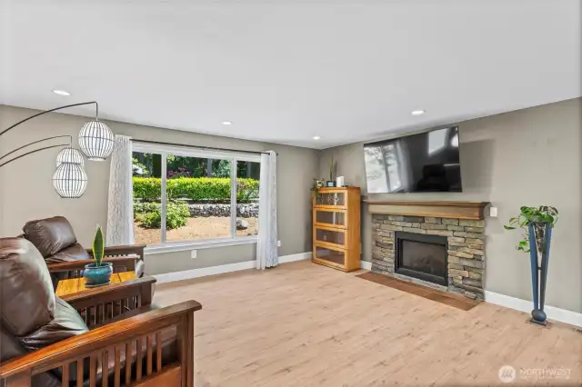 The expansive living room window bathes the open floor plan with natural light. Notice the gas fireplace, adding a touch of warmth and charm to Northwest winter evenings.
