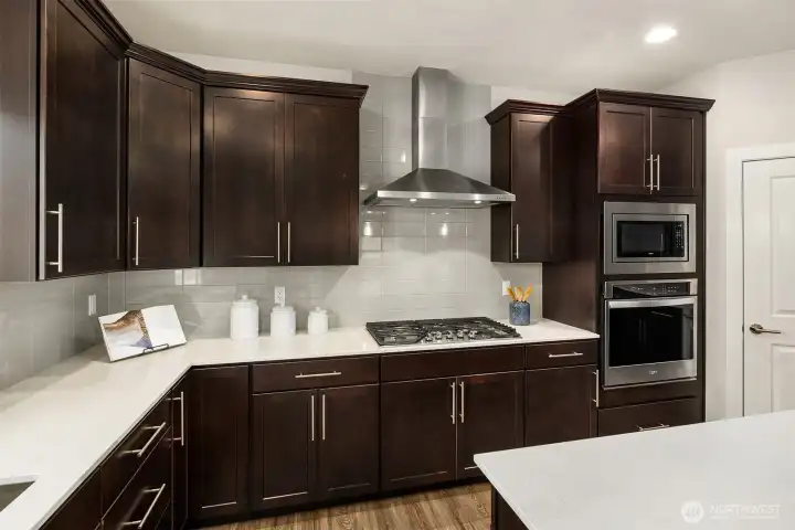 Closer view of cooktop, overhead vent, built-in microwave and oven.