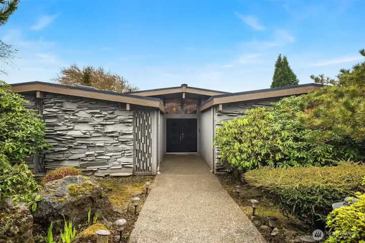 Just a couple steps down from the sidewalk, and then a lovely level entry welcomes you to this sleek 1961 Magnolia home with Primary Suite + 2 beds/1 bath all on the main floor.  Chunky basalt intersects with a vertical MOD wood screen detail, leading to the gorgeous original double entry door capped by vaulted clerestory windows.