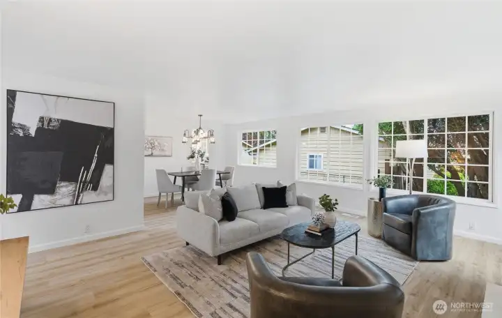Bright, open living and dining space with hardwood-style floors, large grid windows, and a pendant-lit dining area — ideal for everyday living and entertaining.